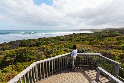 Rear view of man standing on railing against sea