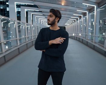 Young man looking away while standing in illuminated covered bridge at night