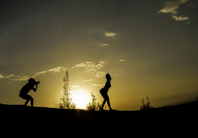 Silhouette man photographing woman on field during sunset