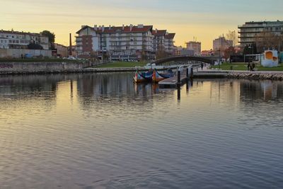 Boats in river against buildings in city at sunset