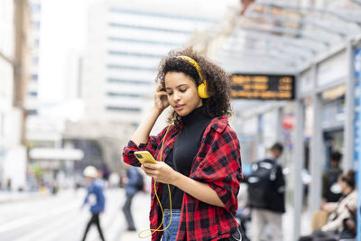 Young woman wearing headphones and using smart phone in city