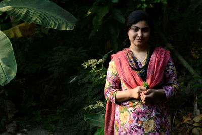 Portrait of young woman standing against plants