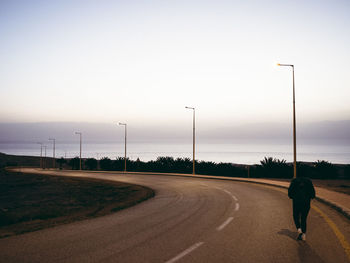 Rear view of man walking on road against sky