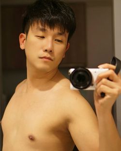 Shirtless mid adult man taking selfie with camera reflecting on mirror at home