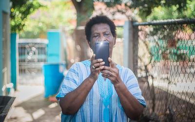 Portrait of young man holding camera while standing outdoors