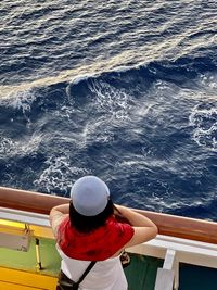 Rear view of woman standing by railing of boat in sea