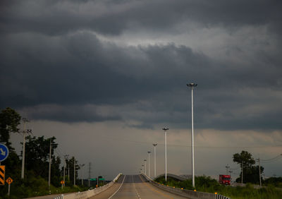 Rear view of man walking on road against cloudy sky