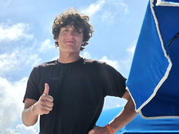 Young man millennial give thumbs up at the beach in summertime.