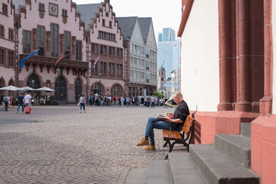 Man sitting in city against sky