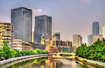 Modern buildings by river against sky in city