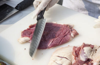 Cropped image of butcher cutting beef on board at table