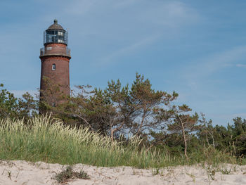 Lighthouse amidst trees and buildings against sky