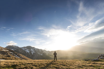 Rear view of man standing on mountain peak against sky during sunny day