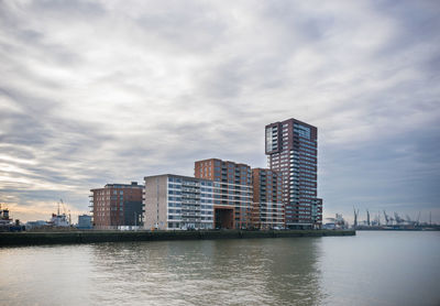 Modern buildings by river against sky in city