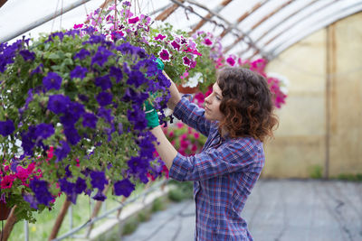 Side view of woman examining flowers in greenhouse