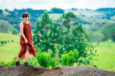 Side view young woman wearing sunglasses walking on mountain against cloudy sky