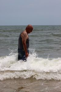 Side view of man standing in sea against clear sky during sunny day