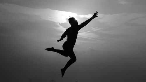 Low angle view of silhouette man jumping against sky