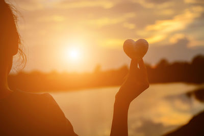 Silhouette woman holding heart shape against orange sky