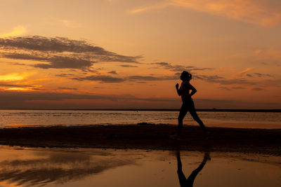 Silhouette woman walking at beach against sky during sunset