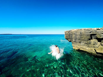 Shirtless boy in sea against clear blue sky