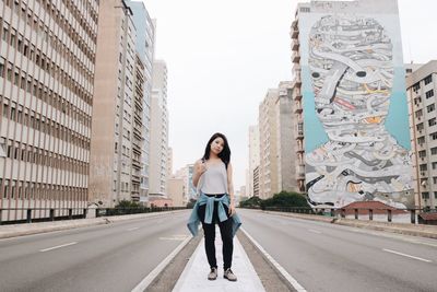 Full length portrait of young woman standing on road in city