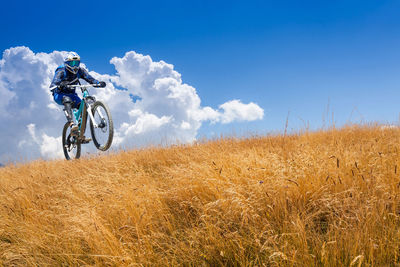 Man riding bicycle on field against sky