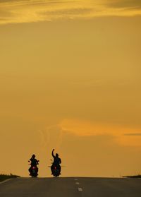 Silhouette people riding motorcycle on beach against sky during sunset