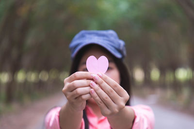 Close-up of woman holding pink heart shape in forest