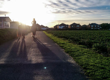 People on field by house against sky during sunset