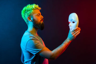 Side view of man holding mask against colored background