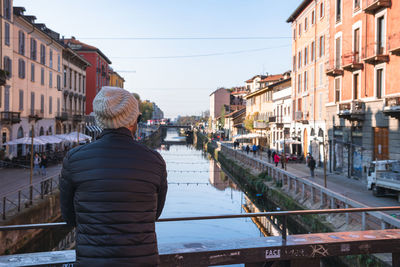 Rear view of man standing on canal in city