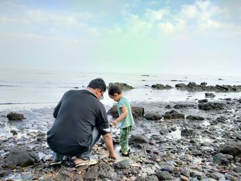 Rear view of father with son at beach against sky