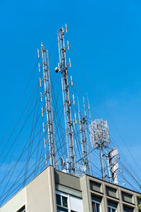 Low angle view of telephone pole against building against clear blue sky