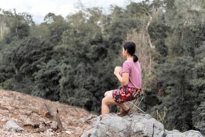 Rear view of woman sitting on rock