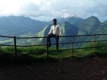 Full length of man sitting on railing against sky