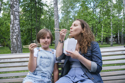 Mid adult mature woman and teenage girl on a summer day in the park has lunch with noodles wok