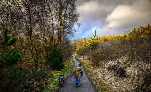 People walking on footpath by road against sky