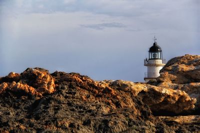 Lighthouse on cliff by sea against sky