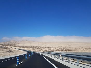 Road leading towards desert against blue sky