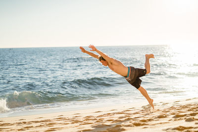 Young man jumping on beach against clear sky