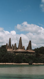 View of temple by lake against cloudy sky