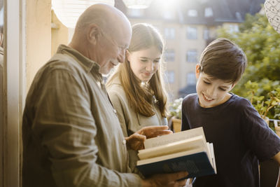 Side view of senior man reading book to grandchildren in balcony