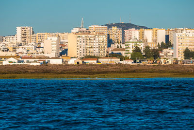 Buildings by sea against clear blue sky