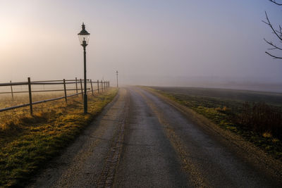 Road amidst field against sky during foggy weather