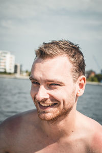 Smiling shirtless man looking away against sea during sunny day