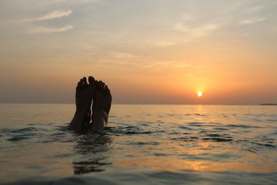 Silhouette men in sea against sky during sunset