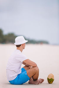 Rear view of woman sitting on beach against sky