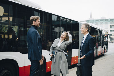 Smiling businesswoman with male coworkers standing against bus in city