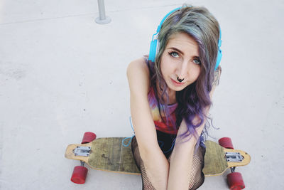 Portrait of young woman sitting on skateboard at park